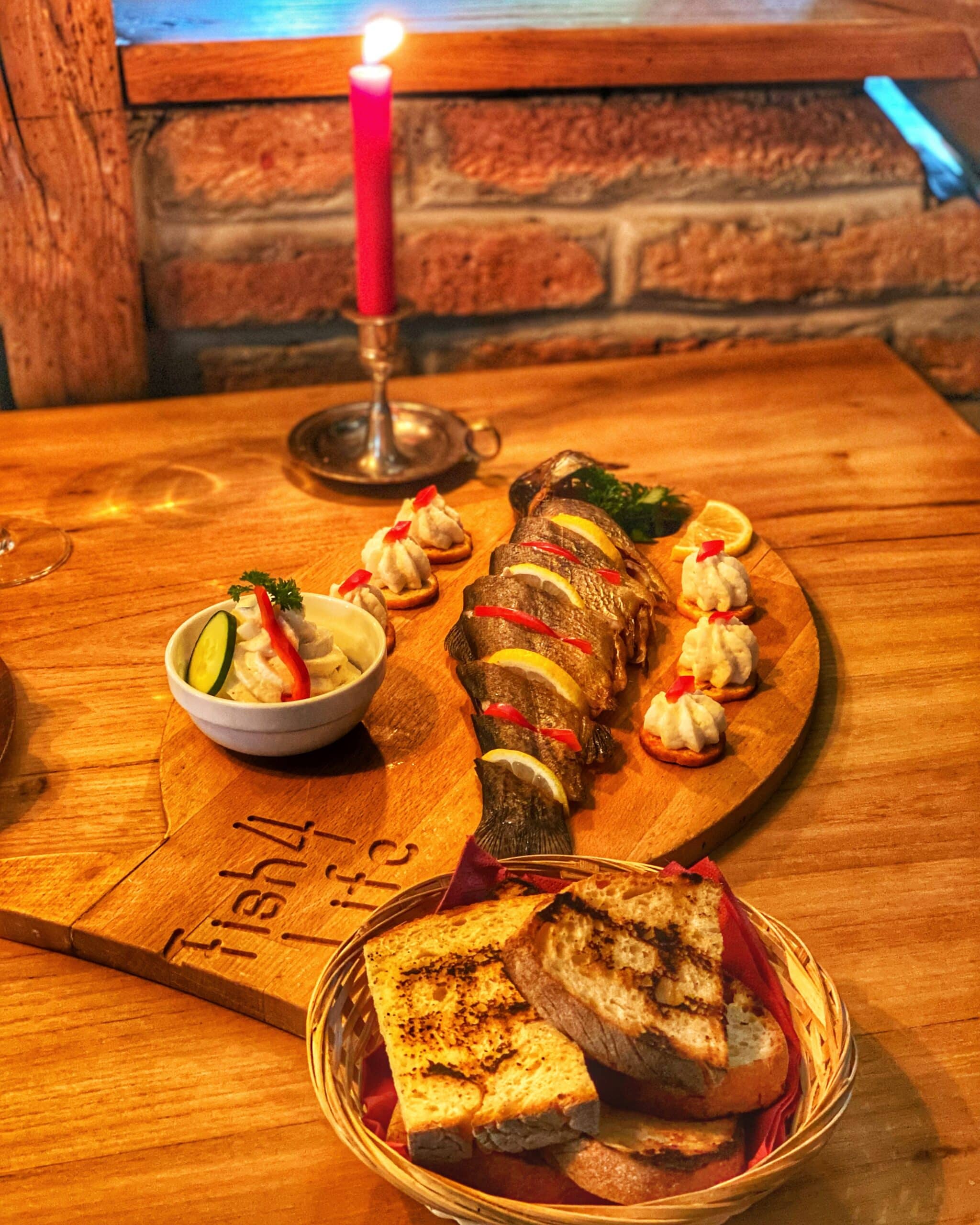 Mesa servida con pescado tradicional, pan y otros ingredientes, acompañada de una vela al fondo, mostrando la gastronomía típica de Transilvania en un ambiente acogedor.