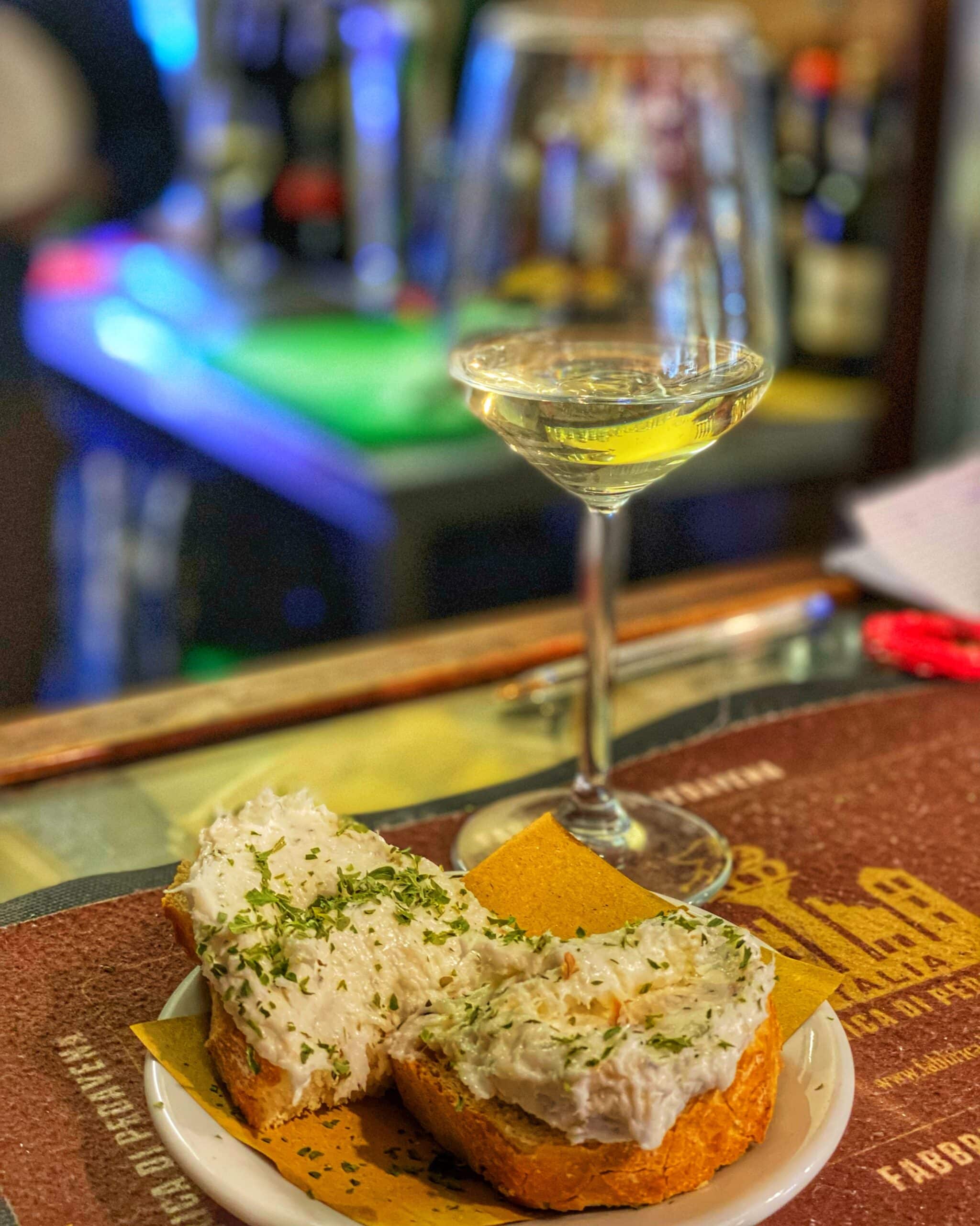 Copa de vino, acompañada de una Tosta con ingredientes típicos de la gastronomía de Venecia, servido sobre una mesa en un ambiente tradicional.