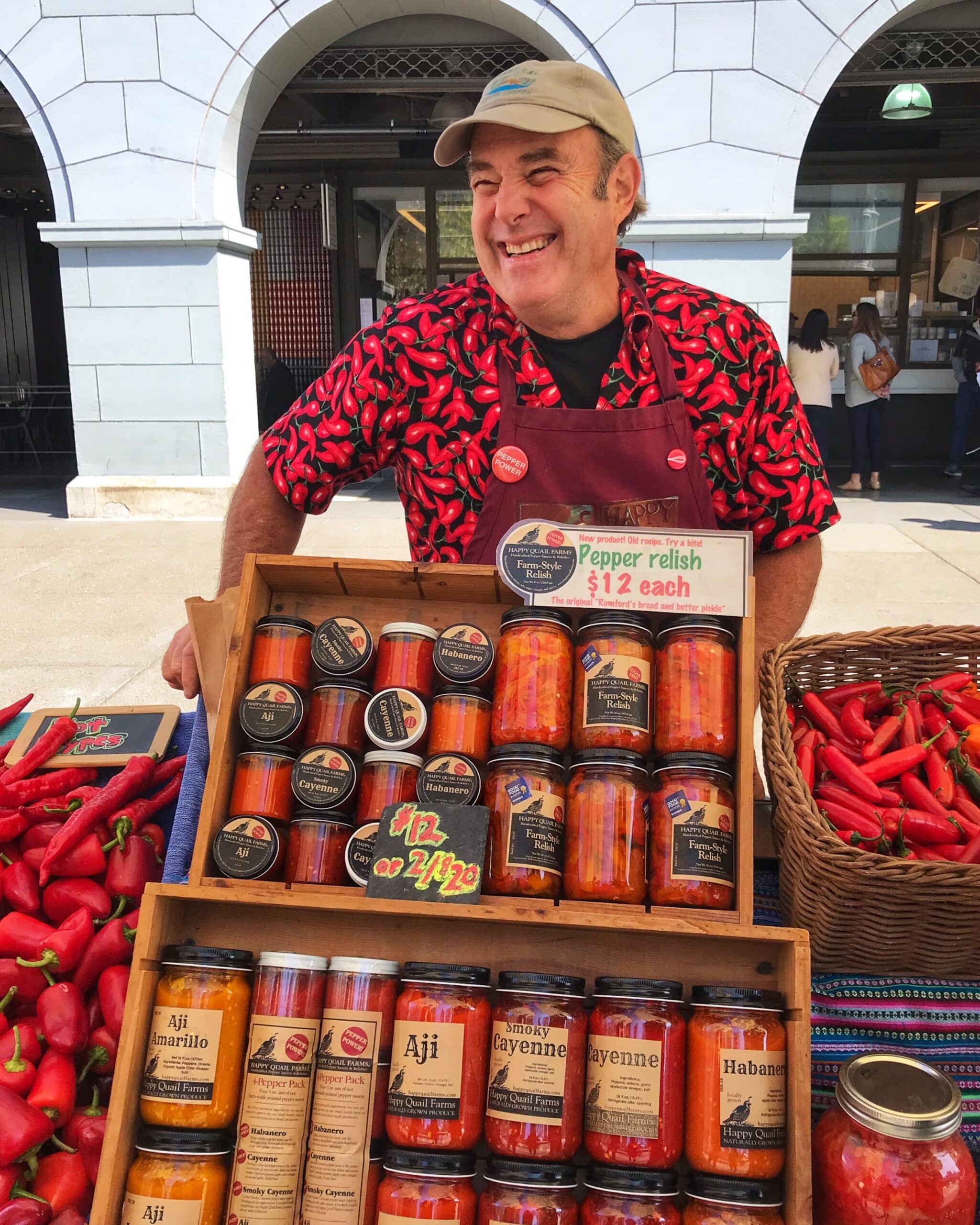 Hombres sonriente, con camisa de pimientos, vendiendo variedad de pimientos frescos y en conserva en un mercado de San Francisco