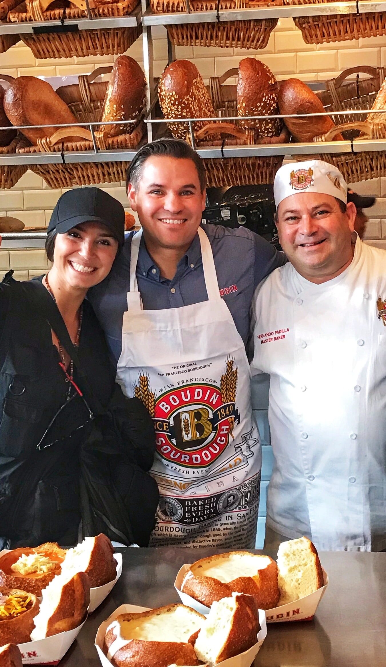 Álvarez de Perea posando con dos personas en una panadería típica de San Francisco, rodeada de panes y productos de repostería artesanal