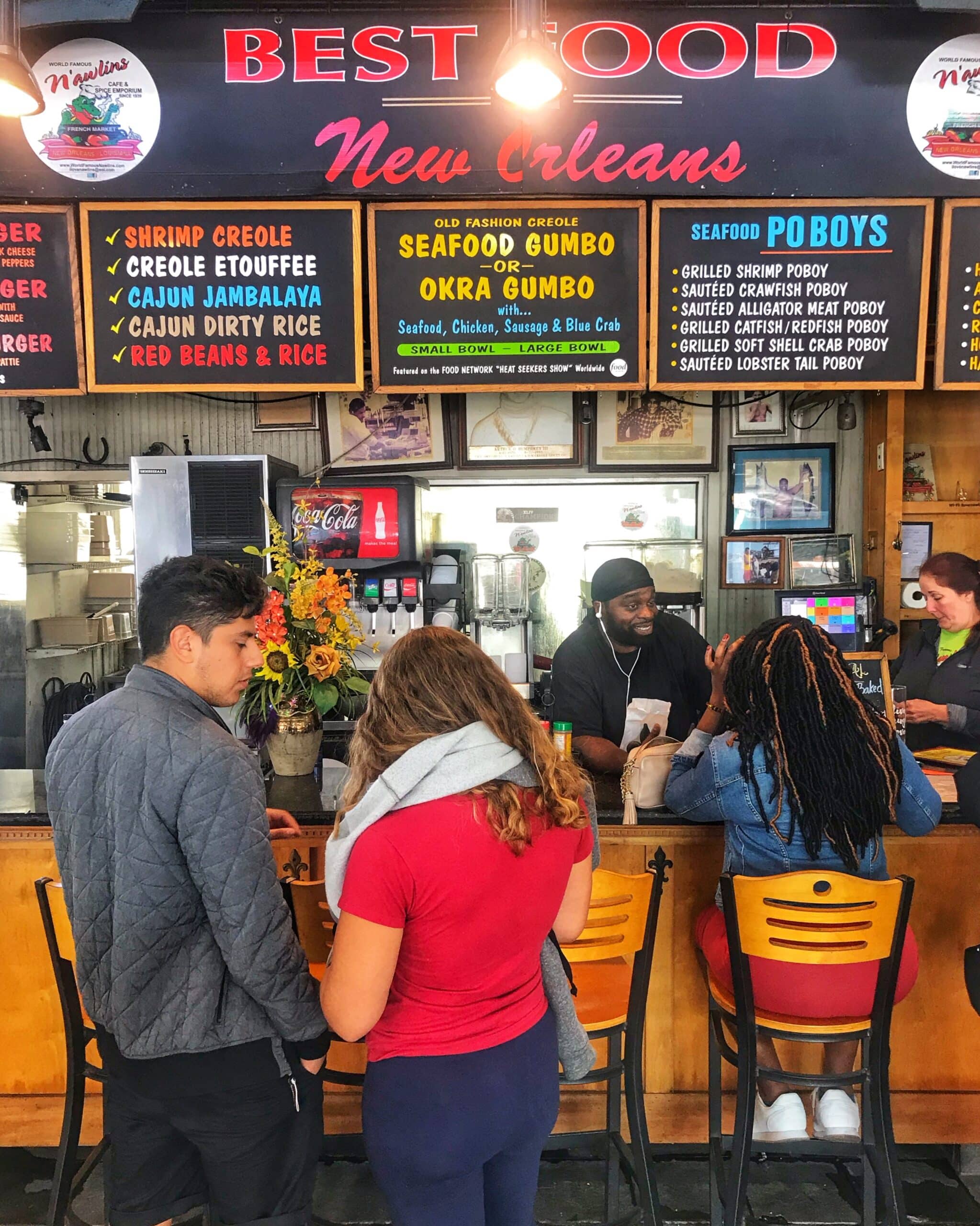 Local de comida en Nueva Orleans con personas sentadas en la barra disfrutando de platos típicos, mostrando ambiente, gastronómico y urbano de la ciudad