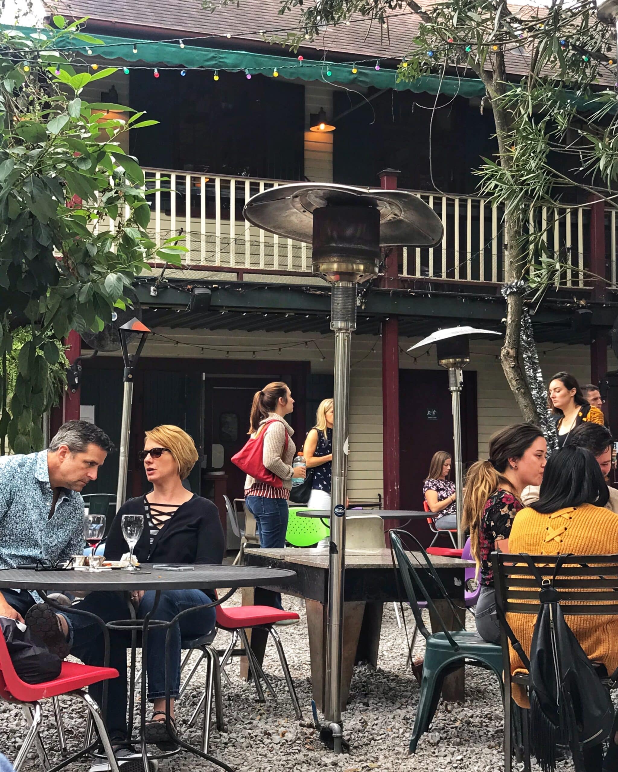 Terraza al aire libre en Nueva Orleans con personas sentadas, disfrutando de comida y bebida, mostrando el ambiente animado y cultural típico de la ciudad de estadounidense