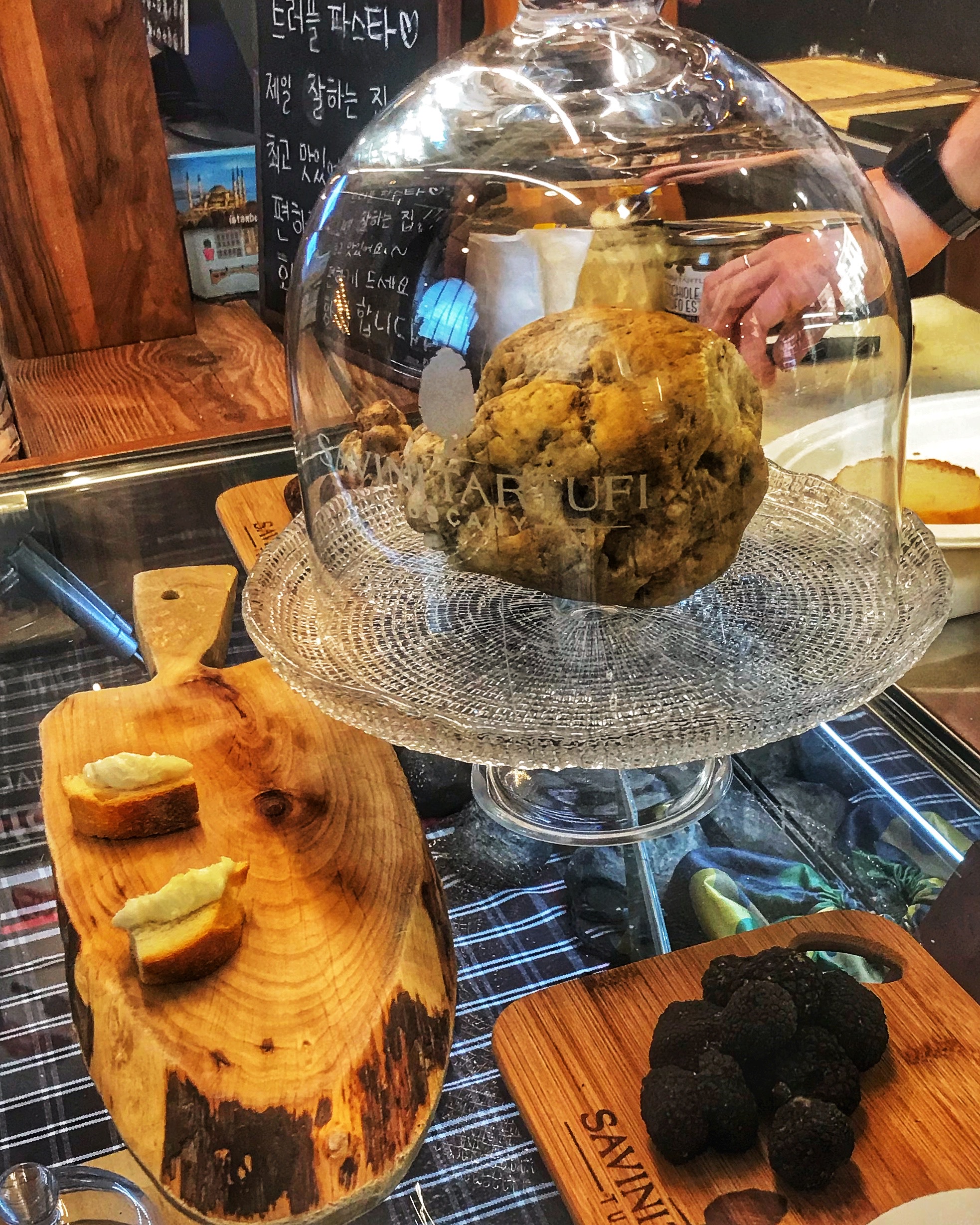 Mostrador con productos gourmet en Roma, incluyendo trufa, quesos y un alimento grande dentro de una urna de cristal, mostrando la gastronomía italiana de lujo y productos delicatessen