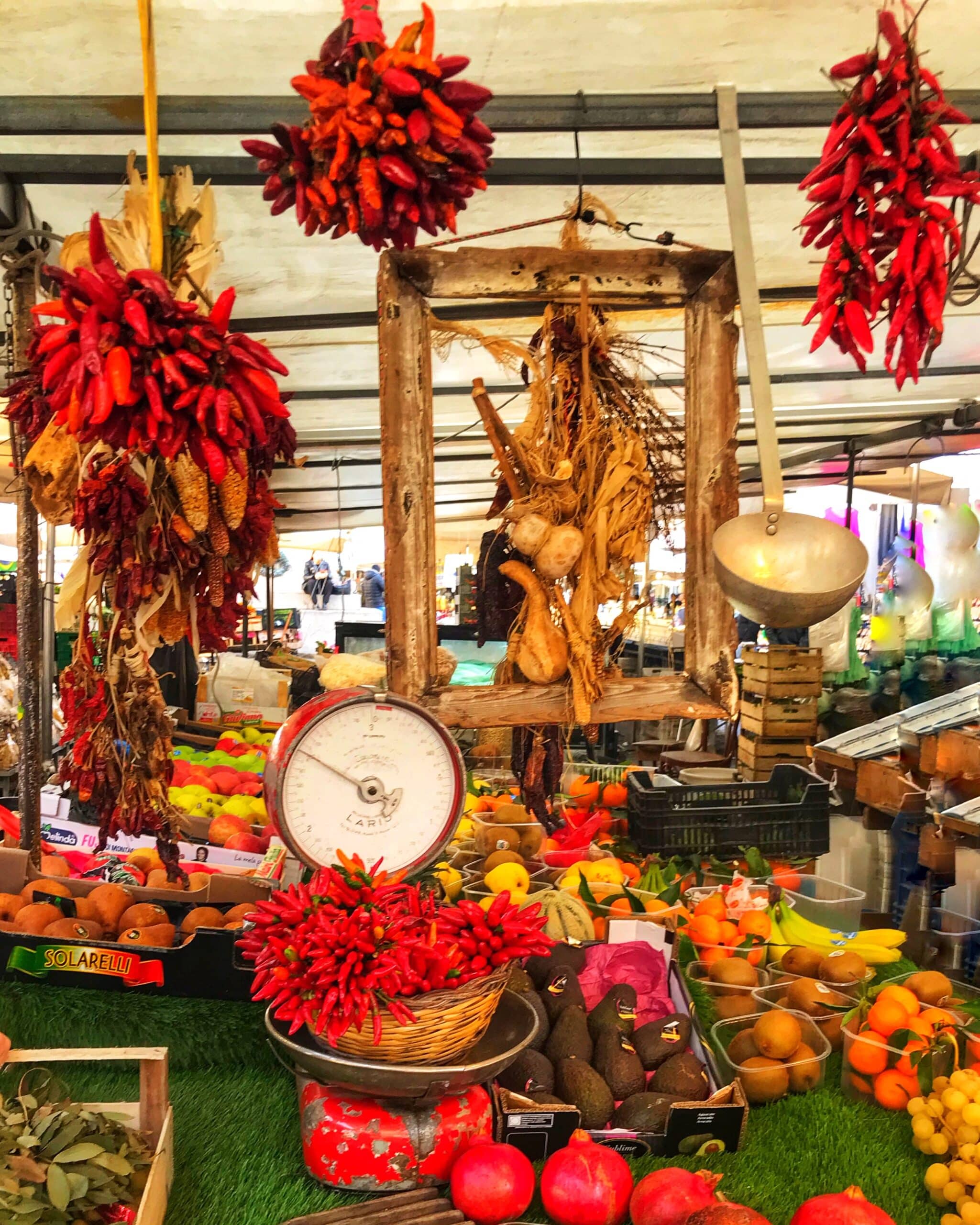 Puesto de frutas frescas en Roma, con variedad de productos coloridos, mostrando kiwis, naranjas y otros frutos típicos en un mercado callejero italiano