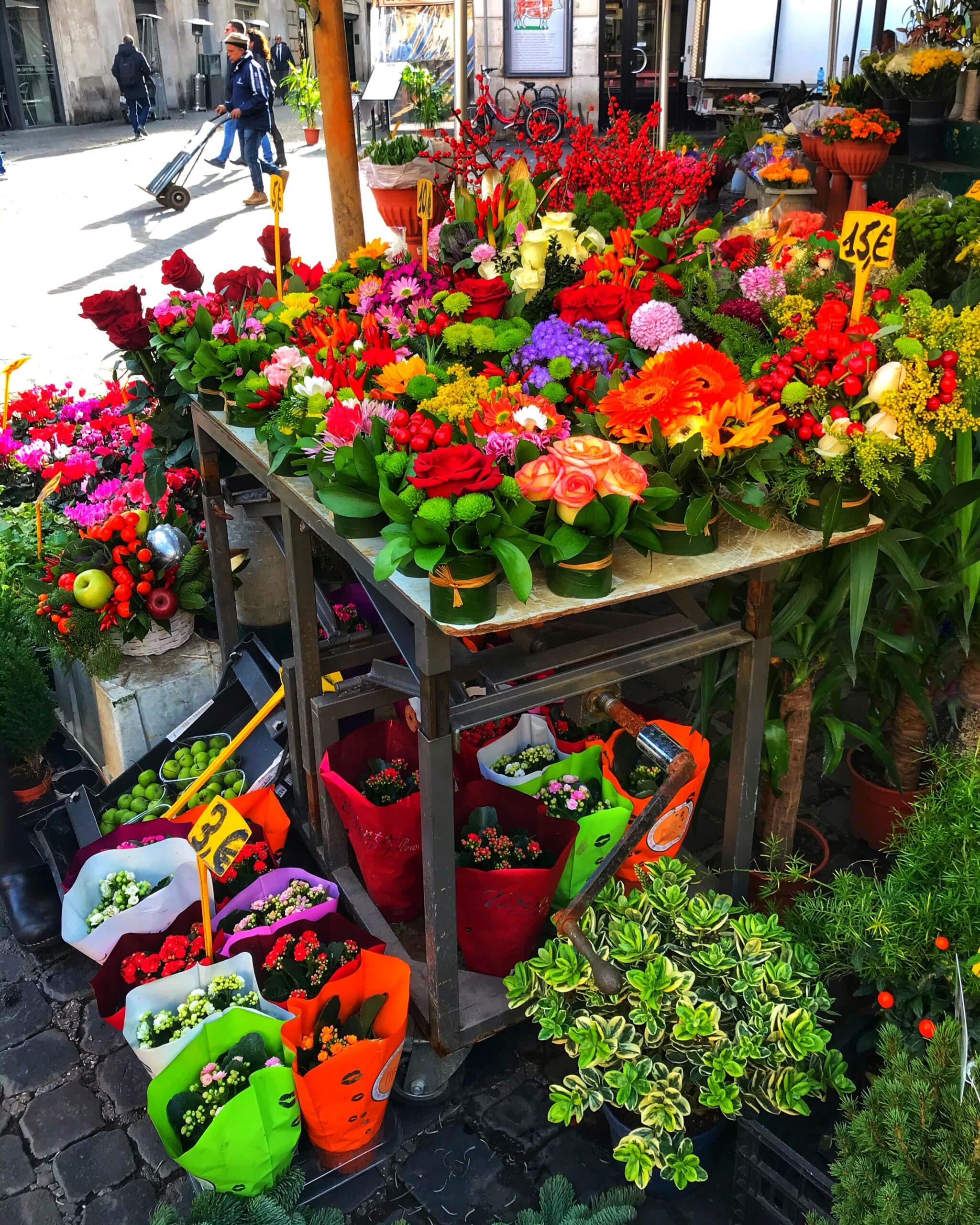 Puesto de flores en Roma con ramos coloridos y variedad de plantas a la venta, mostrando ambiente urbano y tradicional del mercado callejero italiano