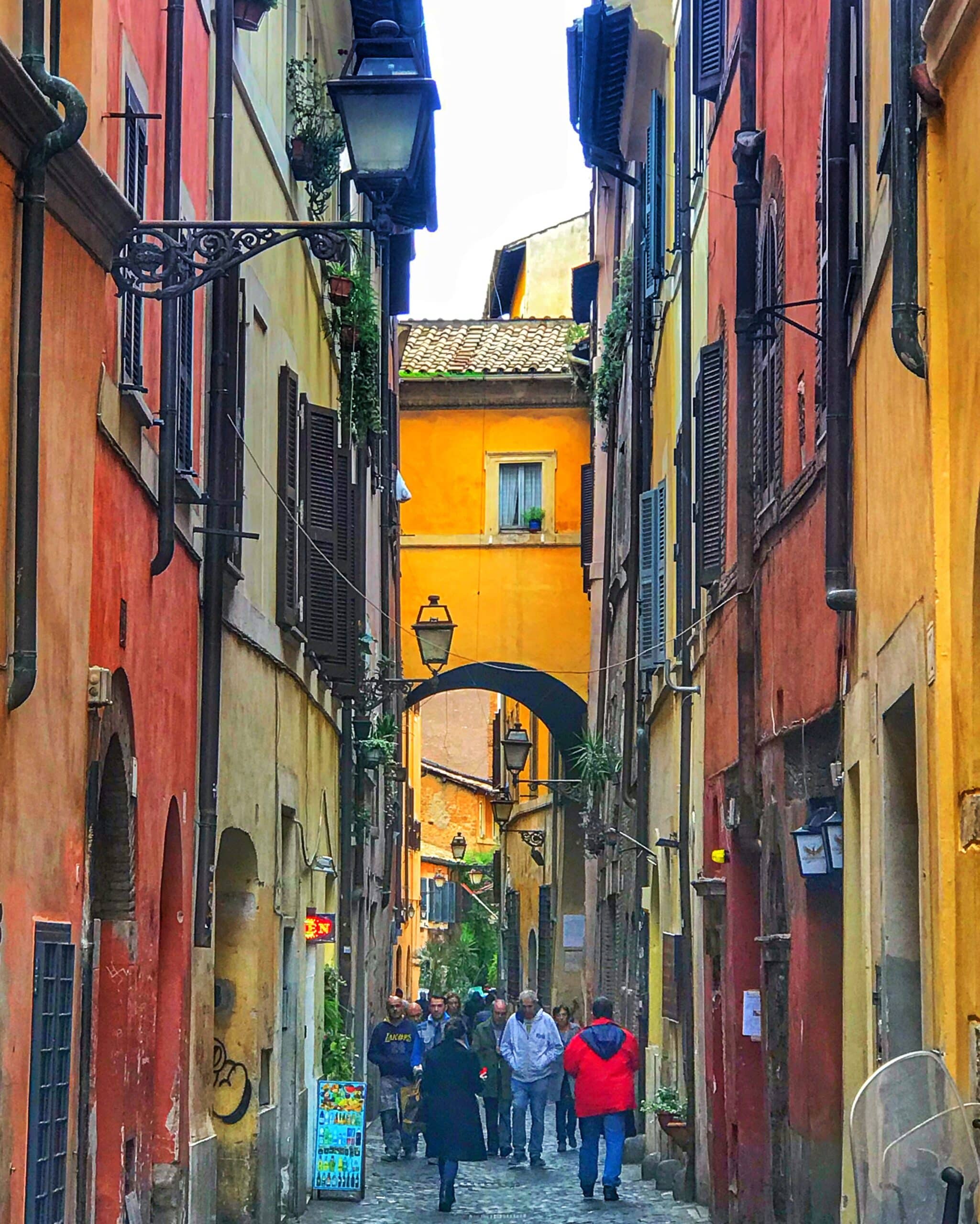 Calle en Roma con edificios de colores y personas caminando, mostrando la arquitectura típica italiana y el ambiente urbano y turístico de la ciudad