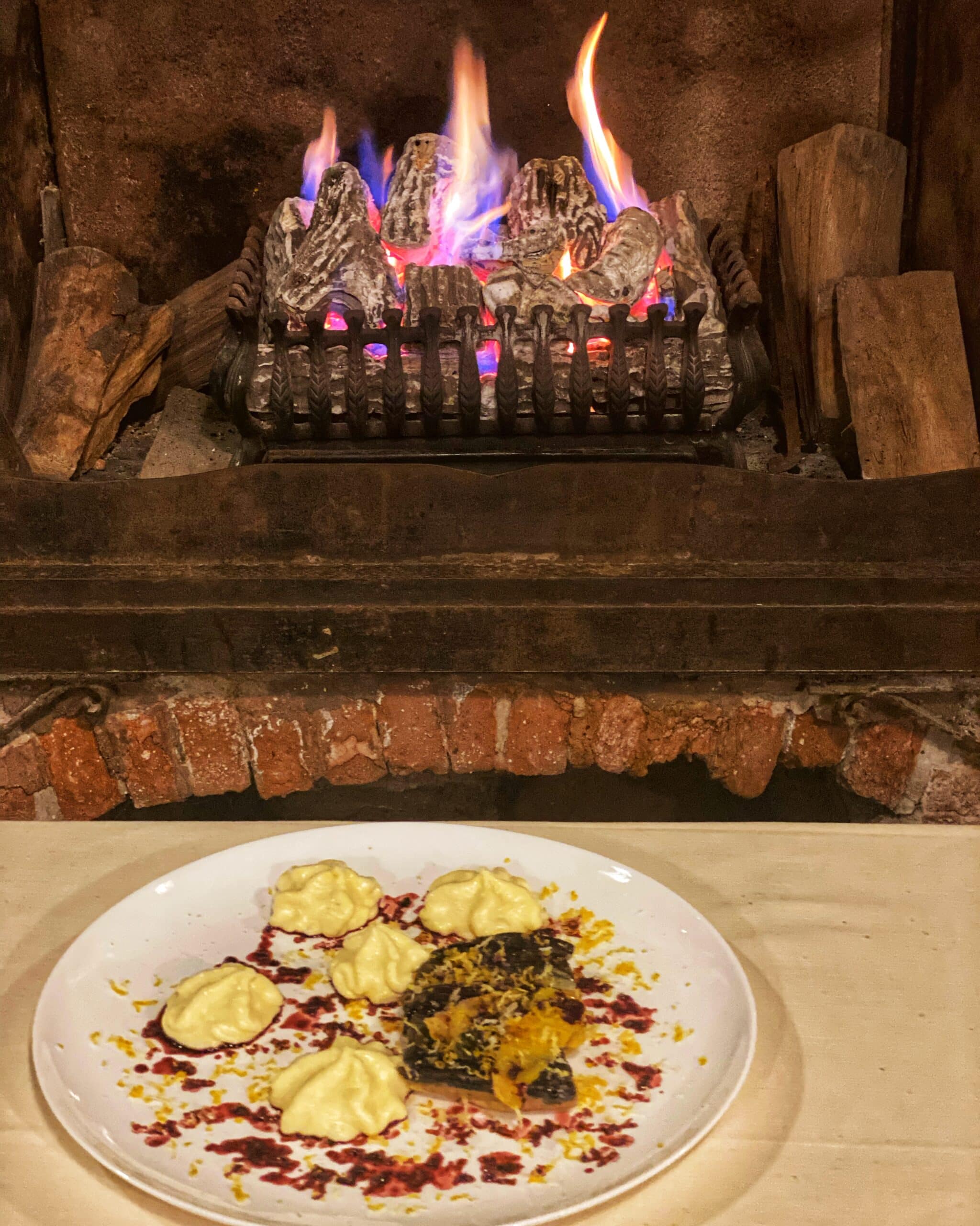 Plato de comida servido, en primer plano, con una chimenea encendida de fondo, que aporta calidez y ambiente típico de un restaurante veneciano.