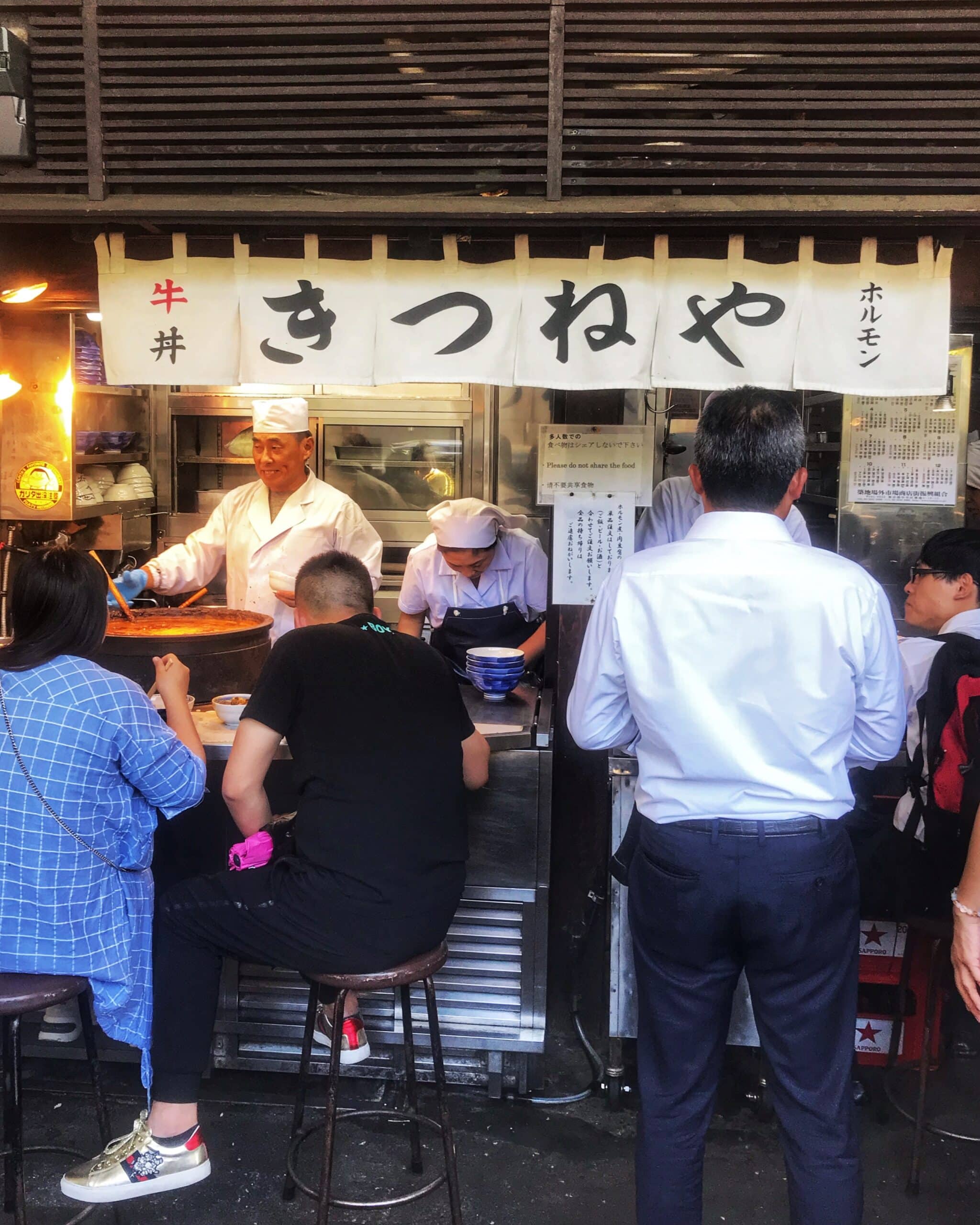 5 varias personas frente a un puesto de comida, típica japonesa en Tokio, observando y comprando platos tradicionales en un mercado o cayo concurrida