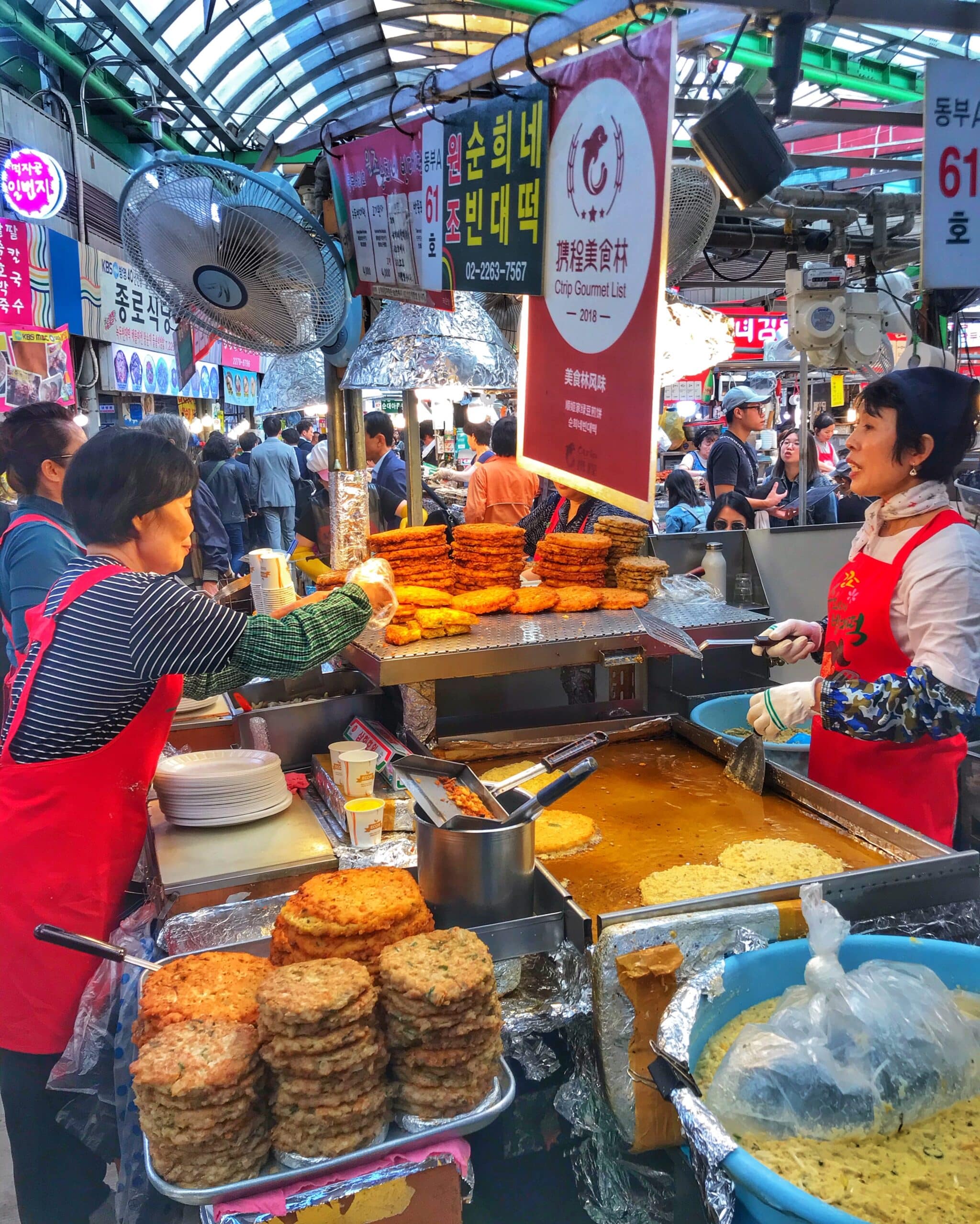 Puesto de comida en un mercado de Seúl, mostrando alimentos frescos y típicos coreanos en un ambiente animado y concurrido de mercado urbano