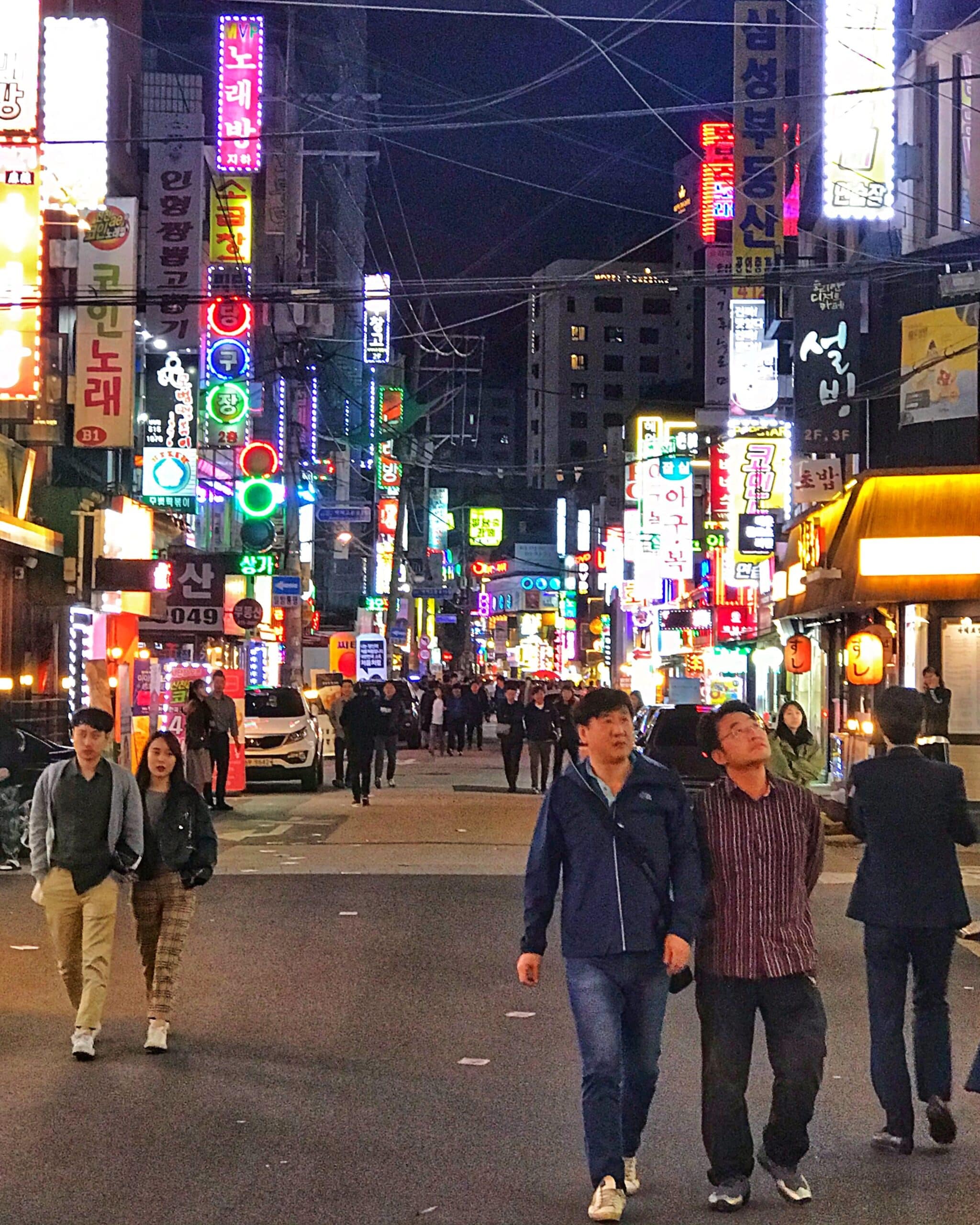 Iluminada de noche en Seúl con personas caminando entre luces de neón, mostrando el ambiente urbano y nocturno de la ciudad coreana