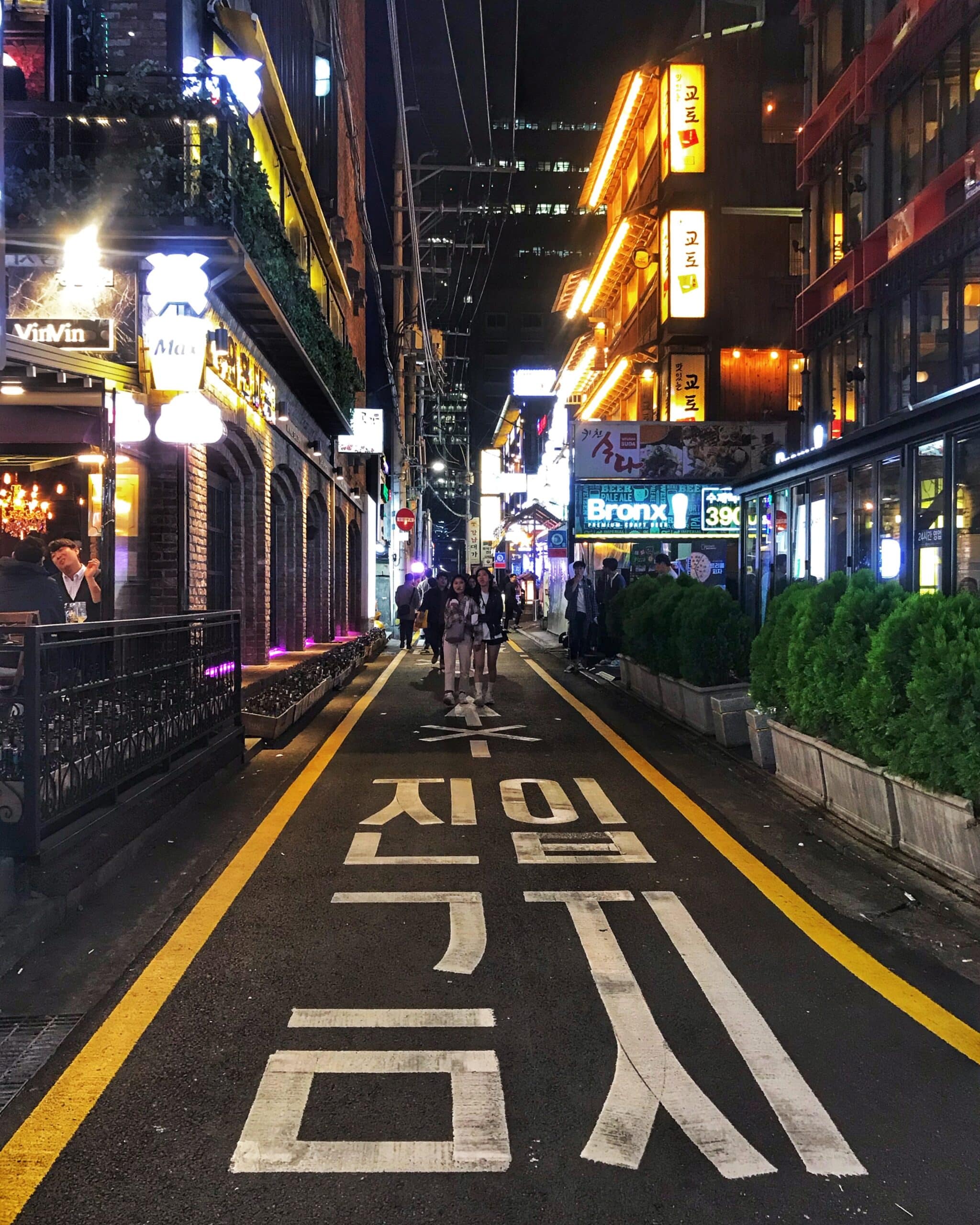 Calle iluminada de noche en Seúl con personas caminando entre luces de neón, tiendas y restaurantes, mostrando el ambiente urbano y nocturno de la ciudad coreana