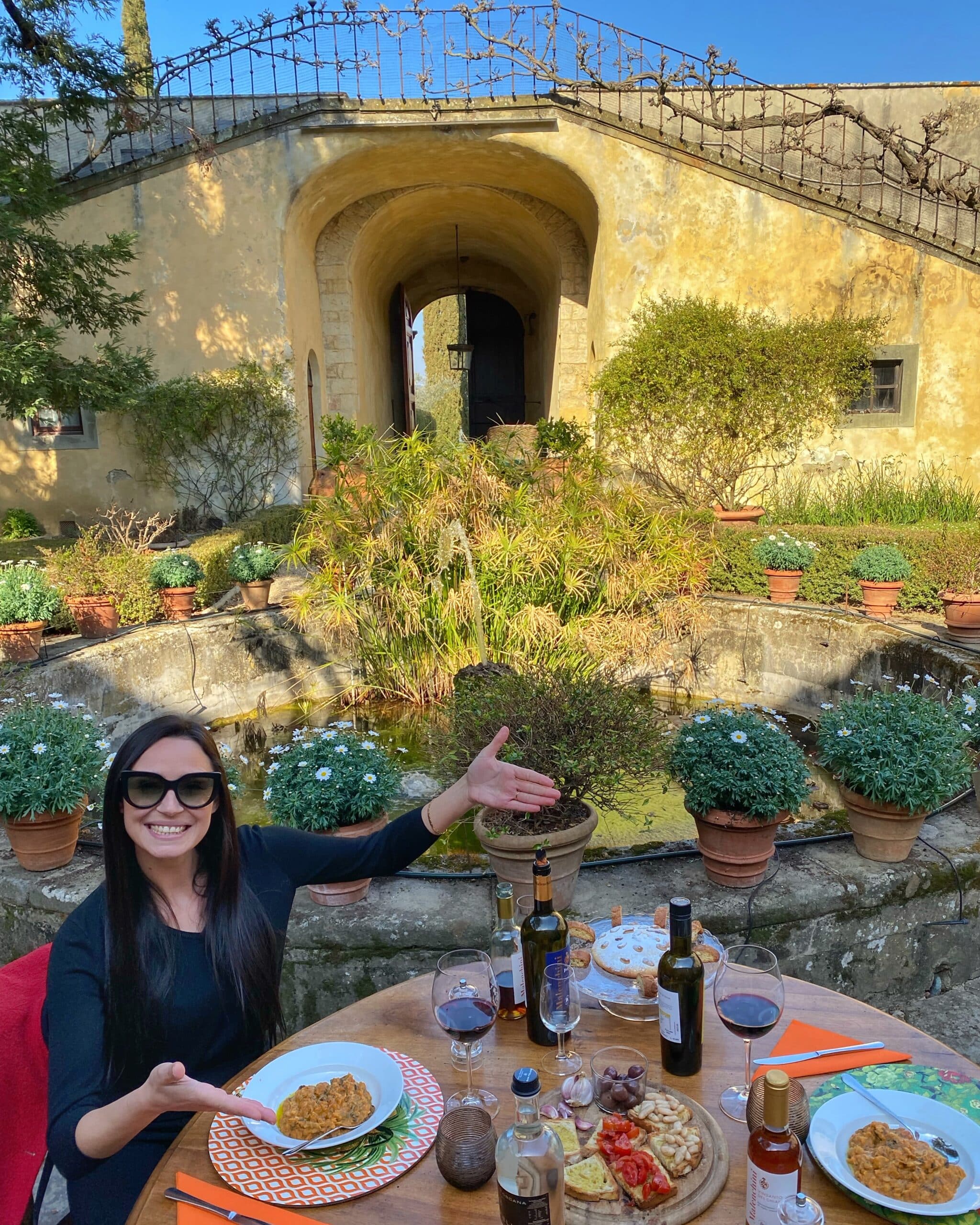 Persona degustando, platos tradicionales toscanos al aire libre con un edificio histórico y una fuente de fondo, mostrando la gastronomía y el ambiente de la región.