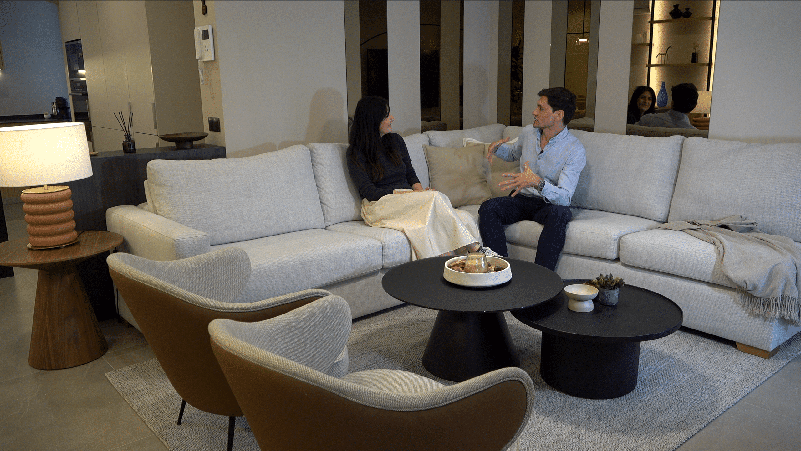 Arquitecto asesorando a una clienta sentados en un sofá hablando sobre un piso, escena de serie Busco Piso, VidaViva Producciones.